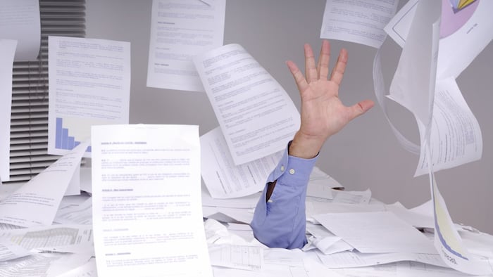 Hand of business man sticking out of a desk full of papers and flying papers