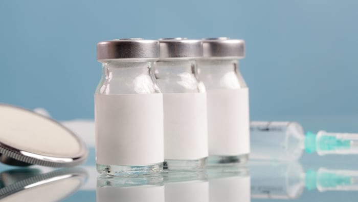 Three vials with blank white labels, syringe in background