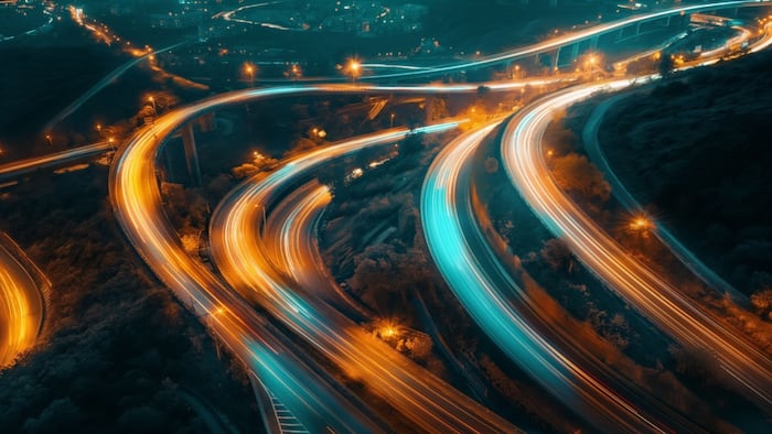 Stunning aerial view of illuminated highway light trails at night, showcasing dynamic movement and urban landscape