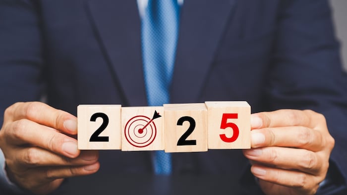 Man in suit holding wooden blocks spelling 2025, with a bullseye replacing the zero.